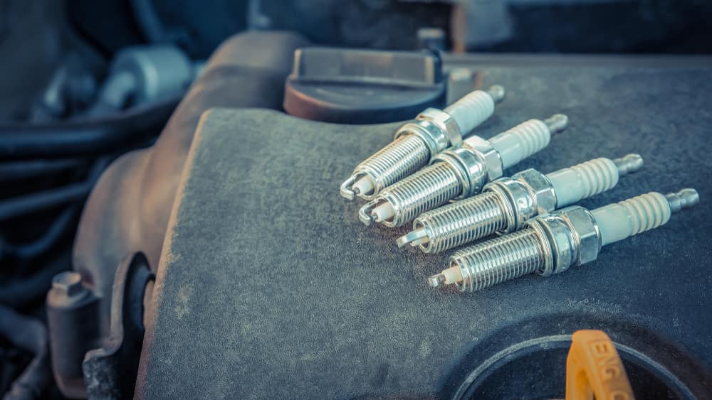 Four-Spark-Plugs-Sitting-on-a-Car-Engine.jpeg Four-Spark-Plugs-Sitting-on-a-Car-Engine.jpeg